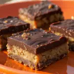 Stacked Oatmeal Fudge Bars with a crumbly oat topping and rich chocolate fudge filling on parchment paper.