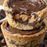 Close-up of two stacked Keto Mini Chocolate Peanut Butter Pies with a golden almond flour crust, creamy peanut butter filling, and a rich chocolate topping. A bite is taken from the top pie, revealing the delicious layers.