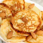 Stack of almond flour pancakes topped with syrup and berries on a white plate