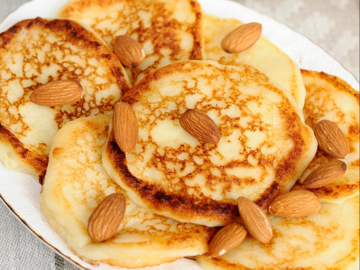 Stack of almond flour pancakes topped with syrup and berries on a white plate