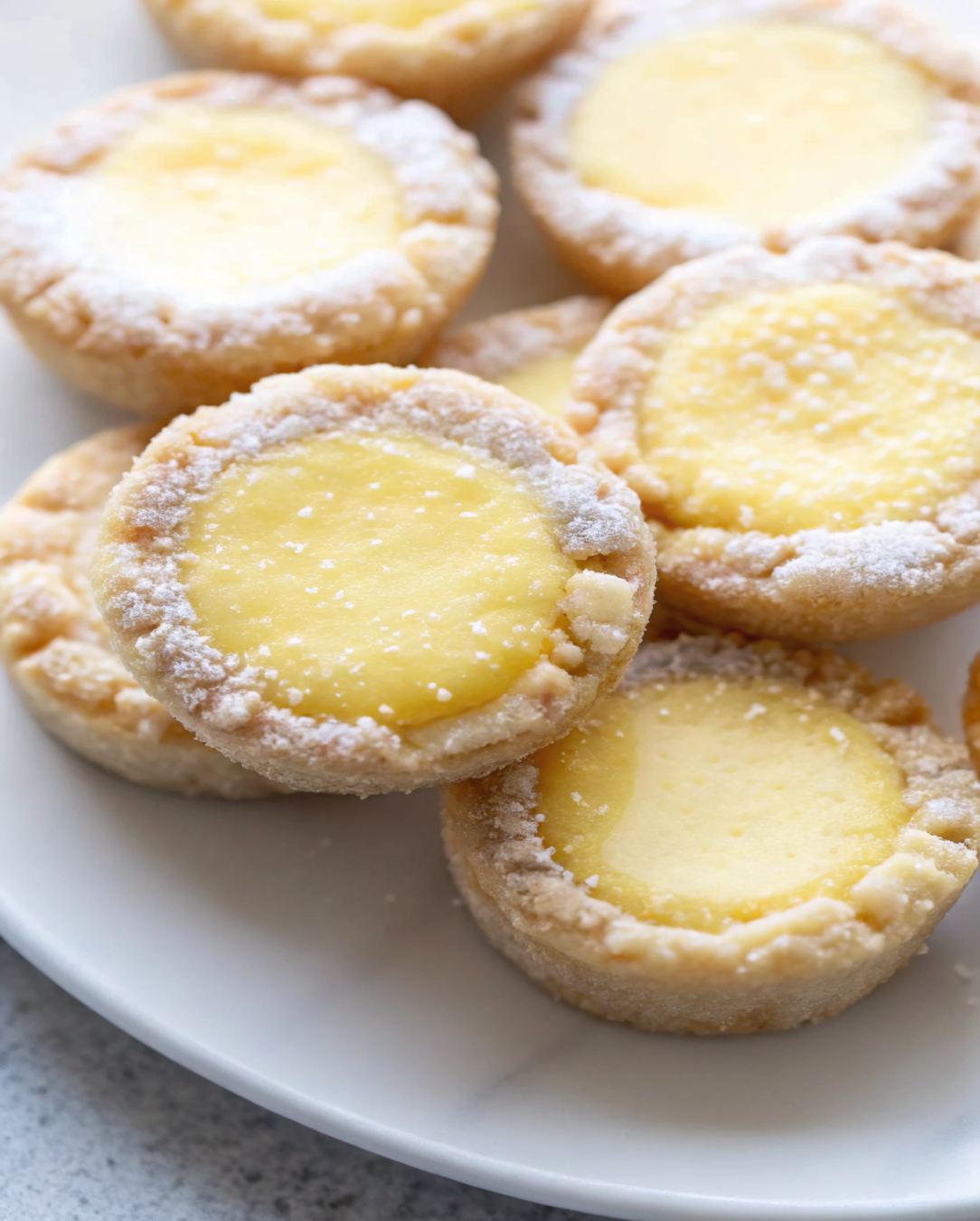 Close-up of soft and chewy keto lemon bar cookies topped with powdered sweetener on a white plate