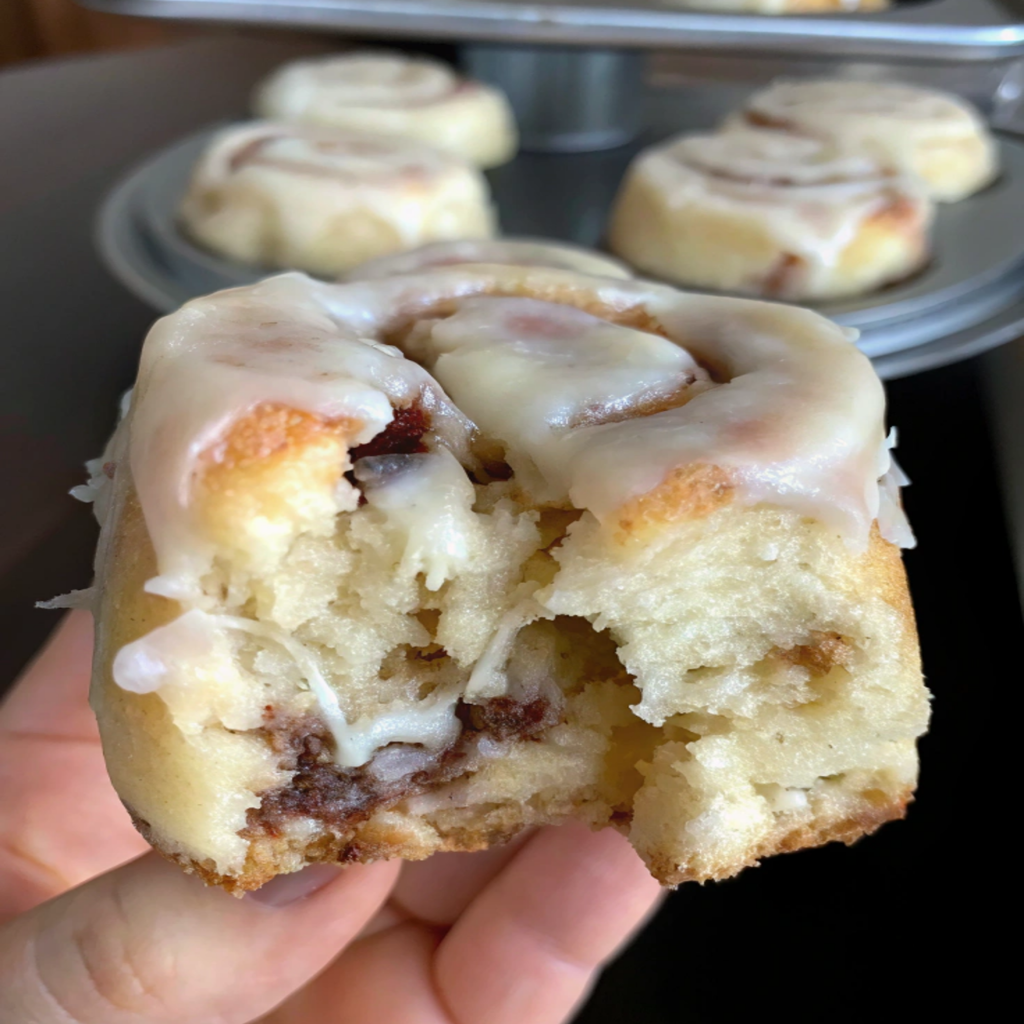A soft and gooey low-carb keto cinnamon bun with cream cheese frosting, held in hand, showing the fluffy texture and cinnamon filling.